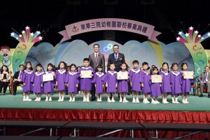 东华三院副主席李鋈麟博士太平绅士（后排右）陪同主礼嘉宾教育局副局长杨润雄太平绅士（后排左）颁发毕业证书予幼稚园毕业学生代表。