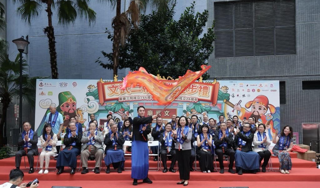 图二为东华三院主席何猷启先生（前排左）从民政及青年事务局局长麦美娟SBS太平绅士（前排右）手中接过出巡令旗，标志著文武二帝出巡正式起步。